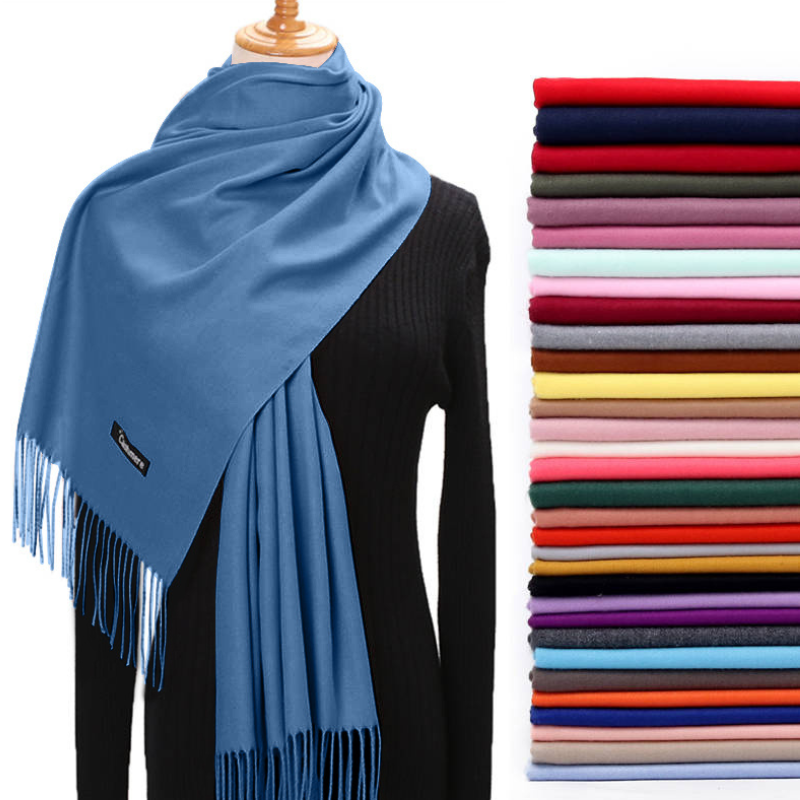 Blue scarf with fringe on a mannequin, next to a stack of folded scarves in various colors.