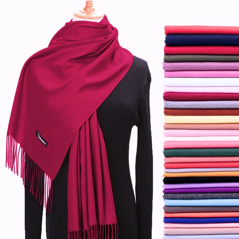 Red scarf on a mannequin with a stack of folded scarves in various colors on a white background